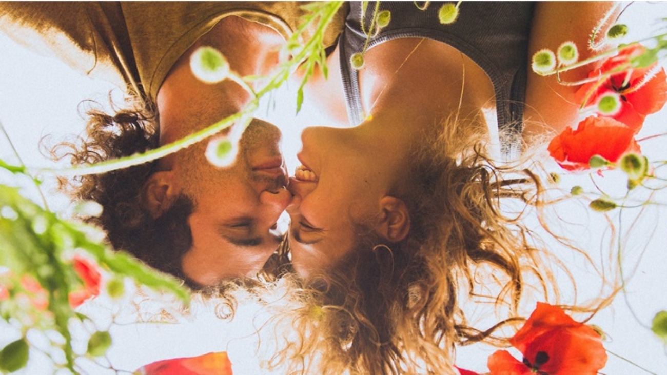 Young happy couple with curly hair enjoying in bright red and yellow blossoming field of poppies in spring