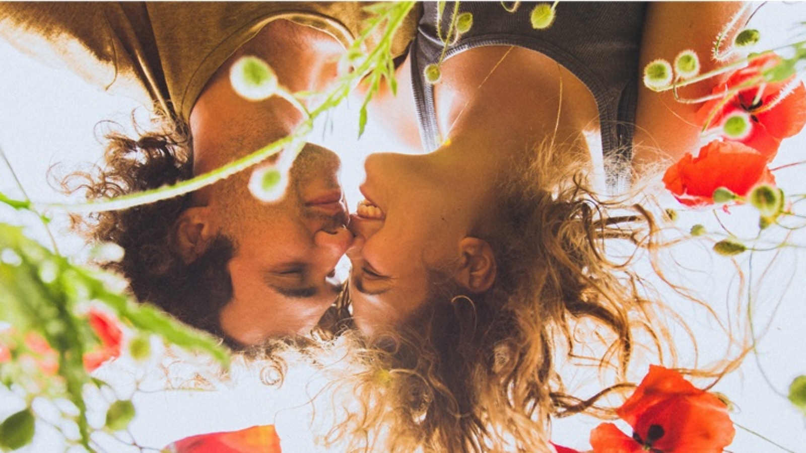 Young happy couple with curly hair enjoying in bright red and yellow blossoming field of poppies in spring